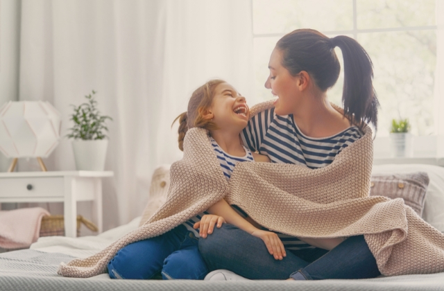 woman and daughter on bed wrapped in blanket laughing