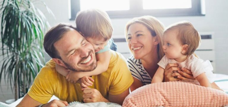 family laying on bed laughing and smiling